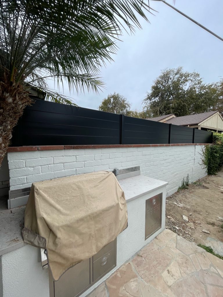 Black aluminum privacy fence with flat top design, surrounded by greenery, showcasing durability and low maintenance features, ideal for residential and commercial use.